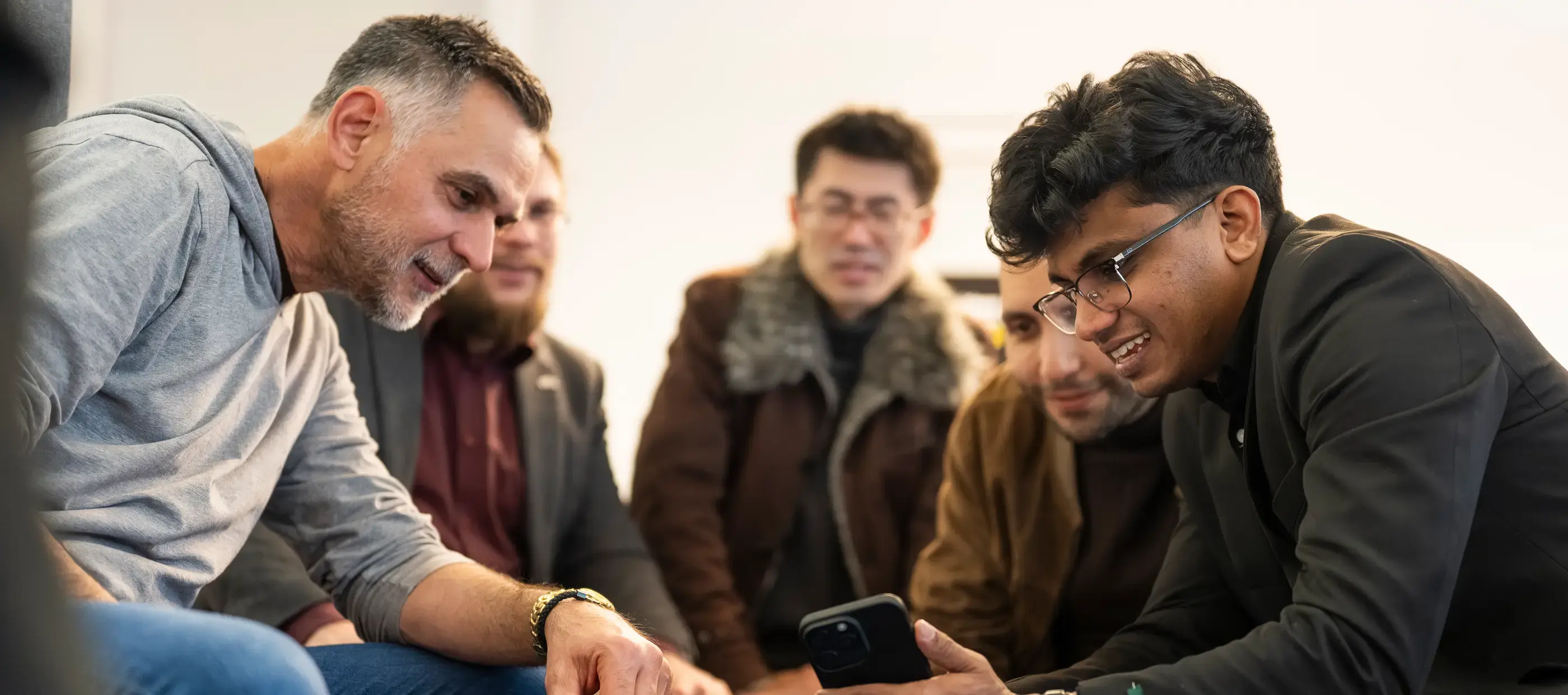 A mentor and students leaning in together around a phone, reviewing work.